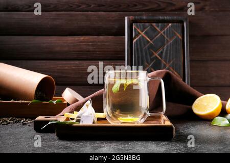 Planche en bois avec une tasse de thé vert savoureux et des ingrédients sur une table sombre Banque D'Images