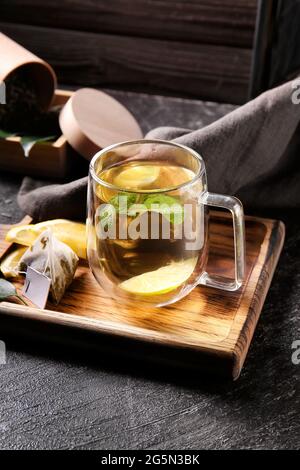 Planche en bois avec une tasse de thé vert savoureux et des ingrédients sur une table sombre Banque D'Images