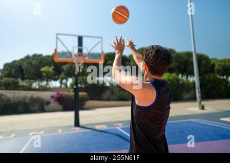 Homme sportif jouant au basket-ball, jetant le ballon sur le terrain de jeu, vue arrière. Prise de vue de précision Banque D'Images