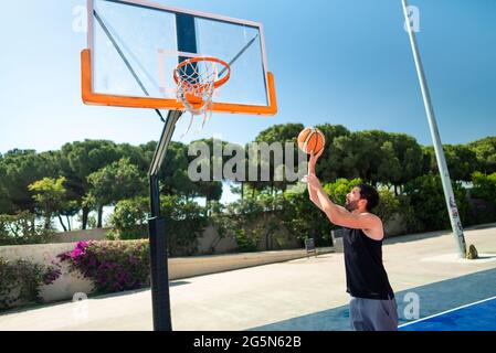 Un sportif masculin jouant au basket-ball lance le ballon sur le terrain de jeu, faisant avec succès la vue de dunk de derrière. Prise de vue de précision Banque D'Images