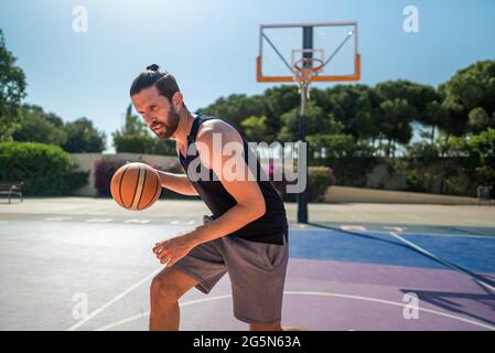 FIT homme jouant au basket-ball extérieur, temps ensoleillé, terrain de jeu moderne. Prise de vue à lentille large Banque D'Images