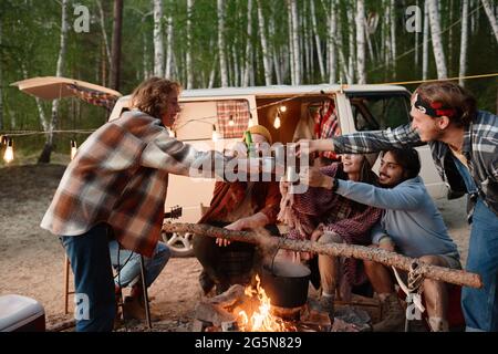 Groupe d'amis qui toaster avec des boissons près du feu pendant le camping dans la forêt Banque D'Images