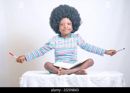 Fille africaine avec un style de cheveux afro montre son amour pour l'éducation comme elle s'asseoir et tenir un stylo et ayant également un livre sur ses tours Banque D'Images