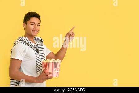 Adolescent afro-américain avec pop-corn pointant vers quelque chose sur fond de couleur Banque D'Images