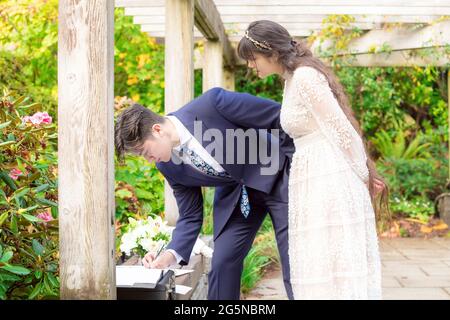 Mariée biraciale et marié à l'extérieur sous pergola en bois signant le certificat de mariage après la cérémonie de mariage Banque D'Images