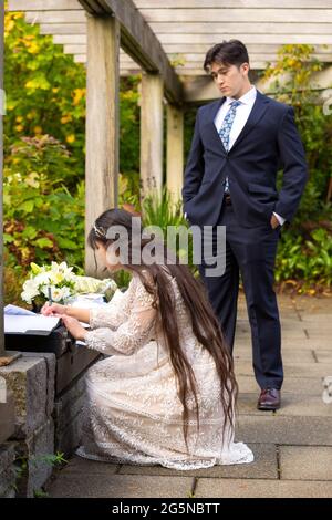 Mariée biraciale et marié à l'extérieur sous pergola en bois signant le certificat de mariage après la cérémonie de mariage Banque D'Images