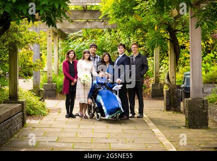 Jeune mariée et marié posant avec la famille à l'extérieur sous une pergola couverte de vigne à côté d'un jeune garçon handicapé en fauteuil roulant Banque D'Images