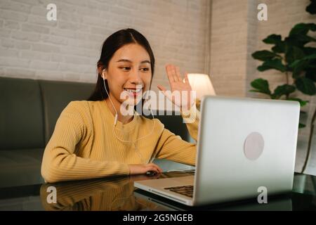 Une jeune femme entrepreneure asiatique qui a réussi à passer la main au client sur l'écran d'un ordinateur portable lors d'une réunion lors d'un appel vidéo tout en travaillant à domicile tard dans la nuit Banque D'Images