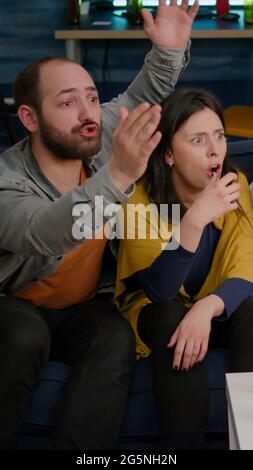 Groupe frustré de personnes multiethniques qui traînaient ensemble tard dans la nuit dans le salon en regardant le football de l'équipe perdre la compétition sportive. Des amis de course mixtes applaudissent à la bière préférée de l'équipe Banque D'Images