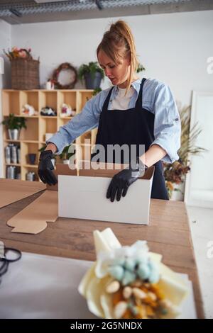 Un jeune fleuriste met une boîte en carton Banque D'Images