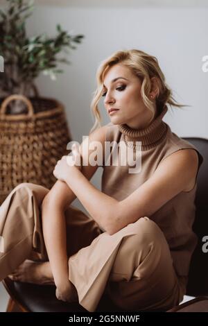 Belle femme pensive se détend dans un intérieur loft moderne. Femme en beige vêtements décontractés. Mise au point sélective douce. Banque D'Images