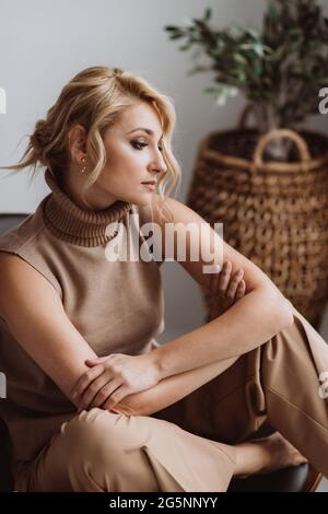 Belle femme pensive se détend dans un intérieur loft moderne. Femme en beige vêtements décontractés. Mise au point sélective douce. Banque D'Images