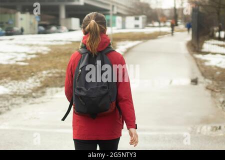 Une fille avec un sac à dos va à l'étude. Une fille dans une veste rouge descend la rue. Une femme va dans le bus. Banque D'Images