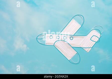 Modèle d'avion fait de masques de protection avec le contour de l'avion contre le fond d'un ciel bleu vif avec des nuages. Déplacement en toute sécurité en avion Banque D'Images