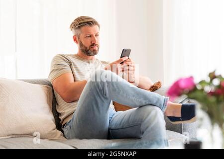 Photo d'un beau homme assis sur le canapé à la maison et messagerie texte. Banque D'Images