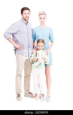 Prise de vue verticale isolée sur toute la longueur de la famille avec un enfant debout ensemble regardant la caméra avec des expressions faciales sérieuses, fond blanc Banque D'Images