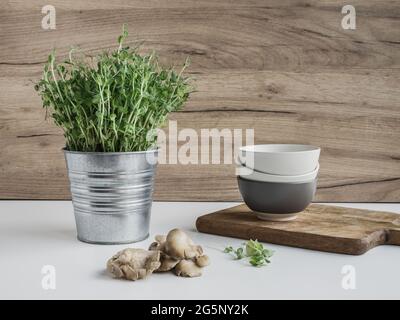 Pousses de pois frais (pisum sativum) en pot de fleurs en métal, champignons et bols sur fond de bois. Banque D'Images