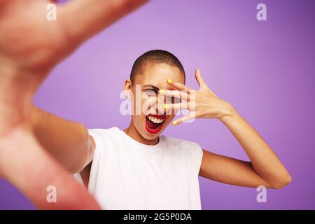 Portrait d'une femme à tête rasée posant avec une expression funky. Modèle féminin tendance sur fond violet. Banque D'Images