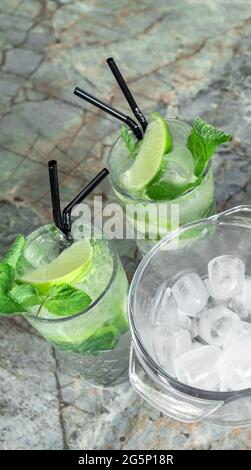 Queue de coktail Gin tonique ou Mojito en verre avec menthe, glace, chaux sur le fond des feuilles tropicales. Banque D'Images