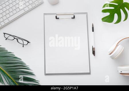 Afficher une liste de notes vide sur l'espace de travail du bureau blanc. Espace de travail indépendant à la maison avec clavier souris lunettes papiers paume feuilles ordinateur portable. Plat Banque D'Images