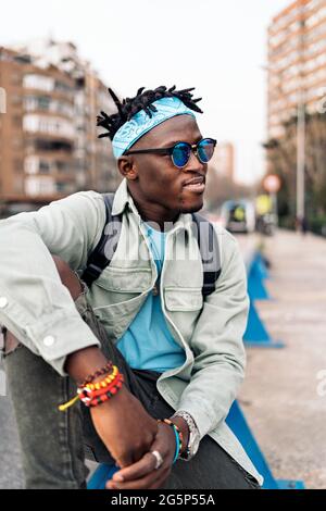 Jeune homme africain confiant, assis dans la rue et regardant sur le côté. Banque D'Images