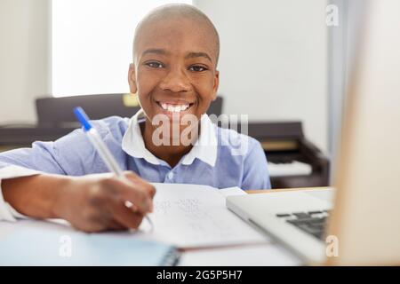 Garçon souriant comme un étudiant faisant des devoirs à la maison en classe à distance Banque D'Images