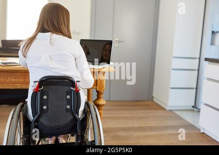 Vue arrière d'une femme en fauteuil roulant utilisant le PC portable du bureau à domicile, symbolisant l'inclusion professionnelle Banque D'Images