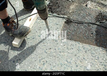 Il enlève l'asphalte avec un marteau à inertie. Retrait de la couche d'asphalte de la route. Le travailleur tient un marteau à inertie. Réparation sur route. Utilisation d'un hammam électrique Banque D'Images