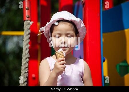 Une fille mange de la glace dans l'aire de jeux. L'enfant mange de la douceur en été. Marchez avec un enfant dans l'aire de jeux. Un pré-chooler au Panama. Banque D'Images