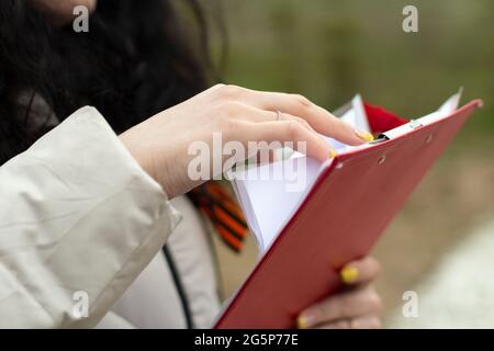 Le secrétaire tient une tablette avec des papiers. La fille tient un papier de bureau avec du texte. Étudier des documents. Les documents imprimés sont croisés à la main. Banque D'Images