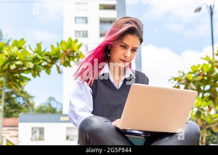 Jeune et belle femme hispanique utilisant son PC portable tout en étant assise sur la paillasse à l'extérieur. Banque D'Images