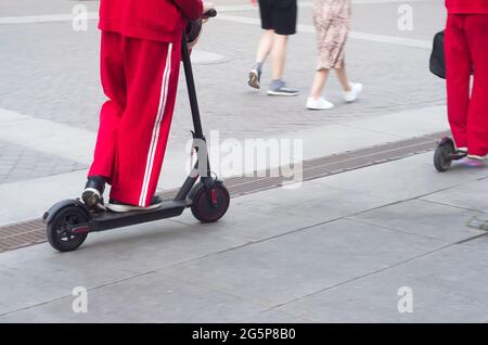 Un groupe d'athlètes sur des scooters électriques se promette le long d'une rue piétonne Banque D'Images