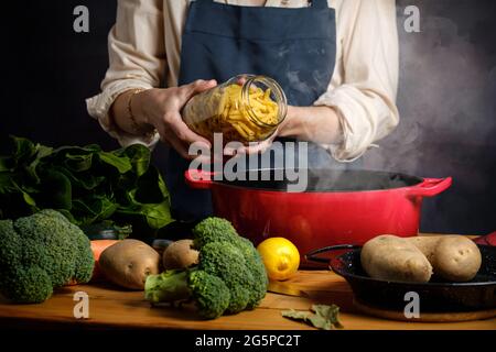 Une femme cuisant des pâtes dans une casserole à la vapeur, sur le brocoli de table, la pomme de terre, la casserole et les épices Banque D'Images
