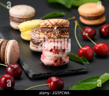 pile de macarons multicolores et de cerises rouges mûres sur fond de bois noir, gros plan Banque D'Images