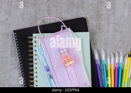 Fournitures scolaires sur divers articles de papeterie colorés à l'école dans des masques médicaux sur le coronavirus Covid-19 Banque D'Images