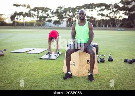 Portrait de l'homme afro-américain en forme s'exerçant à l'extérieur, prenant une pause, assis sur la boîte Banque D'Images