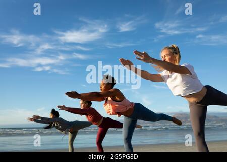 Groupe d'amis féminins divers pratiquant le yoga, s'étirant à la plage Banque D'Images