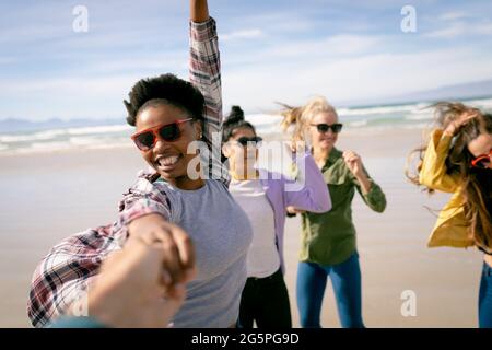 Groupe heureux de diverses amies féminines s'amusant, marchant le long de la plage en tenant les mains et en riant Banque D'Images