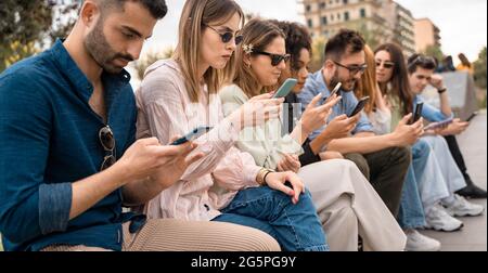 Groupe de jeunes surfant sur Internet regardant le contenu des réseaux sociaux assis à l'extérieur. Des amis qui utilisent des smartphones et des utilisateurs de technologie Banque D'Images