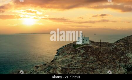 Coucher de soleil sur l'île de Kea Tzia. Grèce, Cyclades. Phare et église d'Agios Nikolaos sur un cap rocheux, drone, vue aérienne. Mer Égée rippée. Été va Banque D'Images