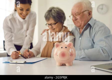 Le couple senior signe un contrat d'hypothèque, de prêt ou d'assurance-vie à la table dans le bureau de banque Banque D'Images