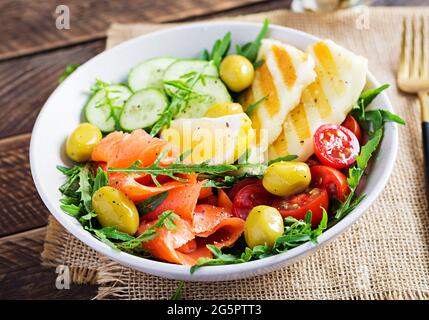 Cétogène, régime céto. Saumon salé, fromage halloumi grillé, tomates cerises et salade de concombres avec olives dans un bol blanc. Une alimentation saine. Banque D'Images