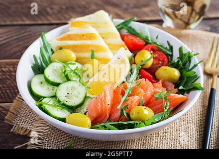 Cétogène, régime céto. Saumon salé, fromage halloumi grillé, tomates cerises et salade de concombres avec olives dans un bol blanc. Une alimentation saine. Banque D'Images