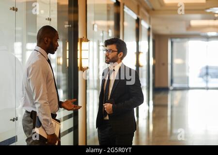 Vue latérale portrait de deux hommes d'affaires discutant dans le hall du bâtiment de bureau, espace de copie Banque D'Images