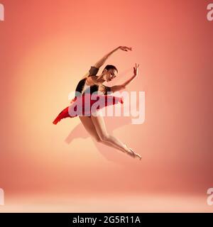 Jeune et incroyablement belle ballerine pose et danse dans un studio rouge plein de lumière. Banque D'Images