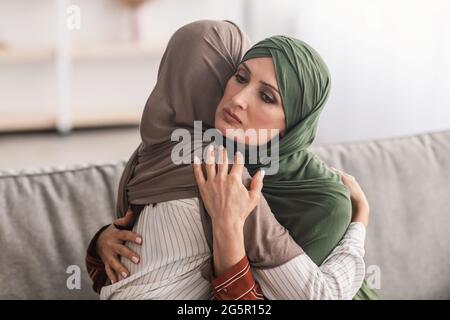 Mère musulmane aînée embrassant une fille adulte malheureuse portant le hijab à l'intérieur Banque D'Images