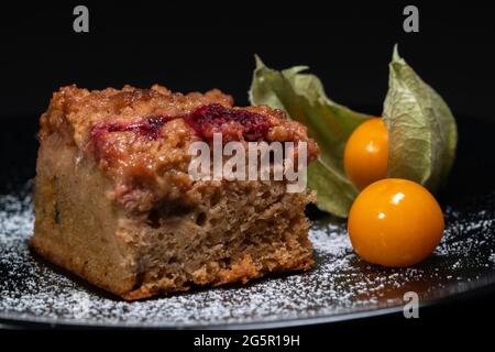 Gros plan d'un gâteau fraîchement cuit avec framboises, jostaberries et rhubarbe sur une plaque noire isolée sur fond noir avec deux physalis mûrs Banque D'Images