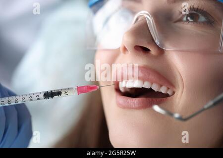 Portrait d'une jeune patiente assise sur une chaise de dentiste avec la bouche ouverte et recevant une injection d'anesthésique Banque D'Images
