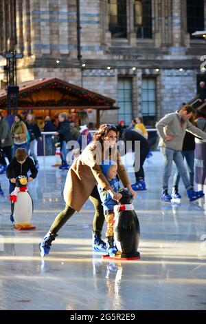 ROYAUME-UNI. ANGLETERRE. LONDRES. LES PARENTS APPRENANT LE PATINAGE SUR GLACE À LEURS ENFANTS SUR LA PATINOIRE MIS POUR NOËL DANS LES JARDINS DE L'HISTOIRE NATURELLE MU Banque D'Images