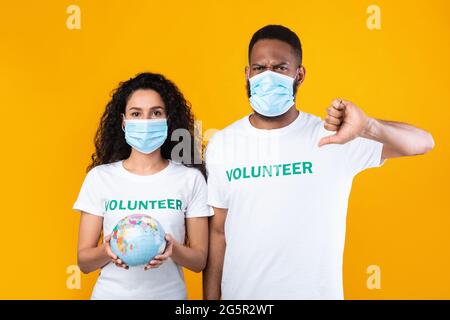 Volontaires portant des masques de visage tenant Earth Globe gesturant Thumbs-Down, Studio Banque D'Images